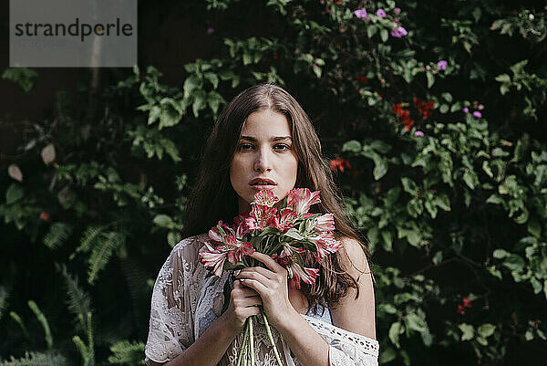 Schöne junge Frau mit Blumen vor Efeupflanzen