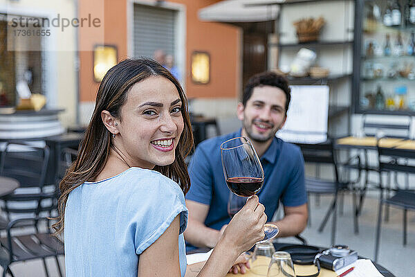 Glückliche Frau trinkt Wein mit ihrem Freund in einem Straßencafé