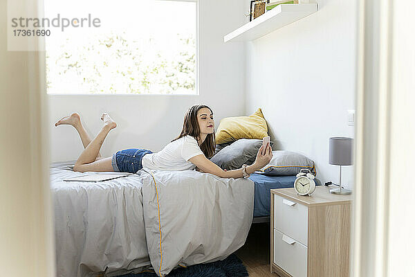 Frau nimmt Selfie durch Smartphone  während auf dem Bett liegend zu Hause