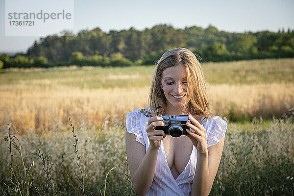 Lächelnde junge Frau schaut in die Kamera  während sie auf einem Feld steht