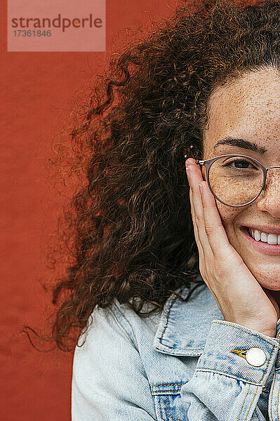 Lächelnde junge Frau mit Brille vor einer roten Wand