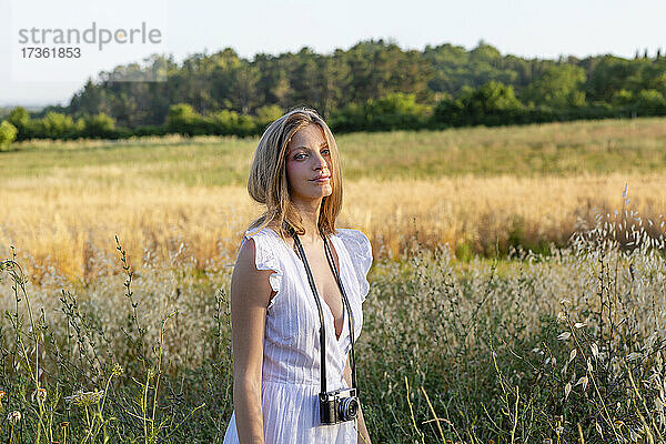 Junge Frau im weißen Kleid mit Kamera im Feld