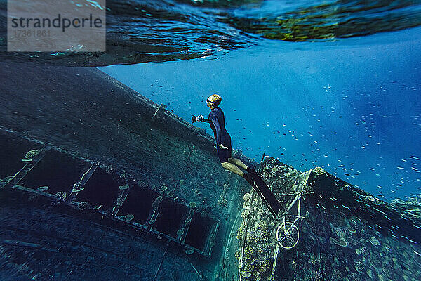 Junger Mann in Taucherflossen schwimmt an einem Schiffswrack im Meer