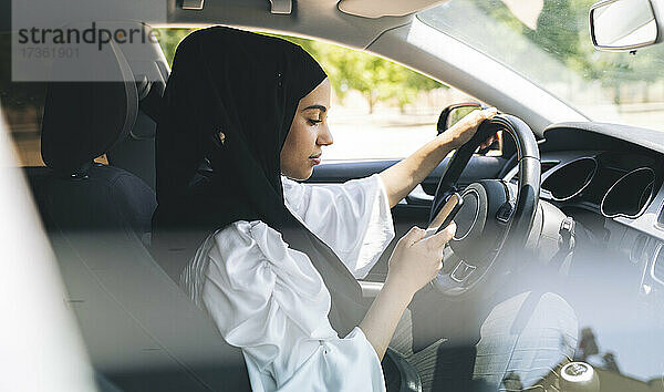 Frau sendet Textnachrichten über ihr Mobiltelefon  während sie Auto fährt