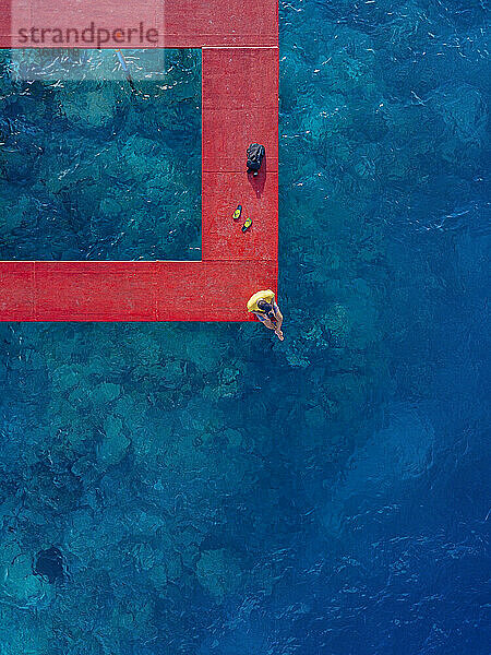 Mann sitzt auf einem roten Steg über dem Meer auf der Insel Thulusdhoo im Kaafu-Atoll  Malediven