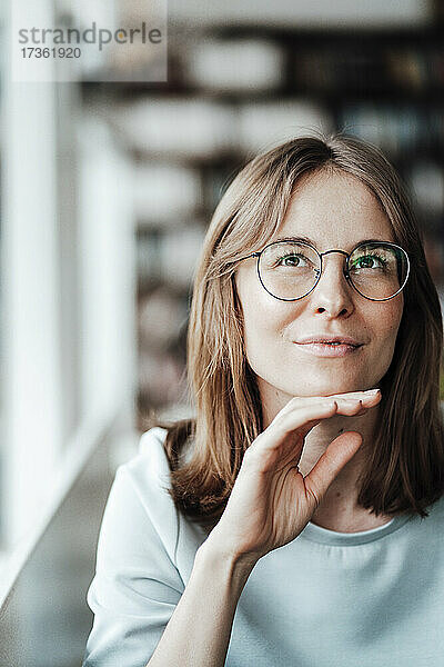 Junge Frau mit Brille sitzt mit der Hand am Kinn in einem Cafe