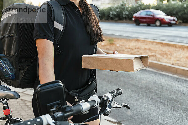 Weiblicher Angestellter  der ein Kurierpaket hält  während er mit dem Fahrrad fährt