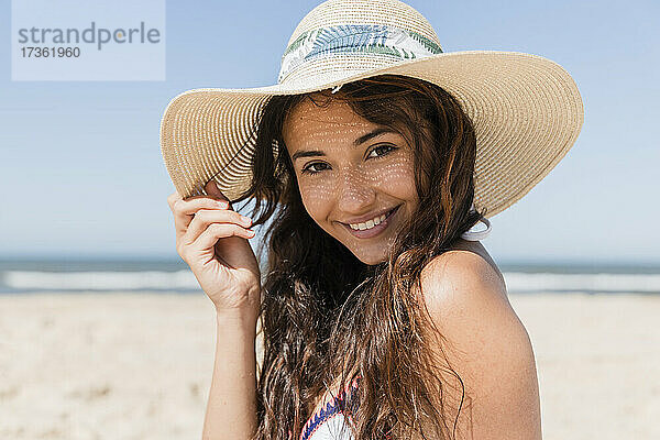 Lächelnde Frau mit Sonnenhut am Strand im Urlaub