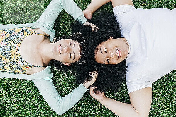 Junge Freundinnen mit Händen in den Haaren liegen im Gras in einem öffentlichen Park