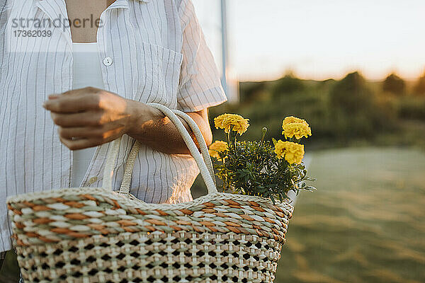 Frau hält Blumen in einer Tasche bei Sonnenuntergang