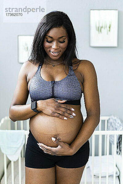 Lächelnde schwangere Frau  die im Schlafzimmer ihren Unterleib berührt