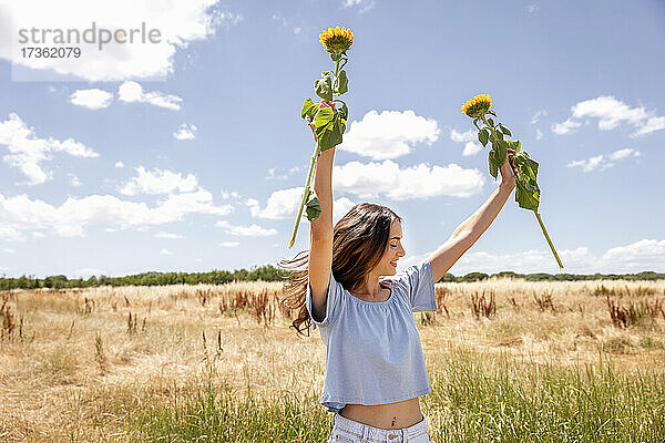 Frau hält Sonnenblumen  während sie im Sommer auf einer Wiese steht