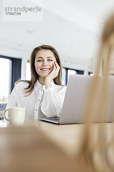 Weibliche Fachkraft mit Hand am Kinn lächelnd im Büro