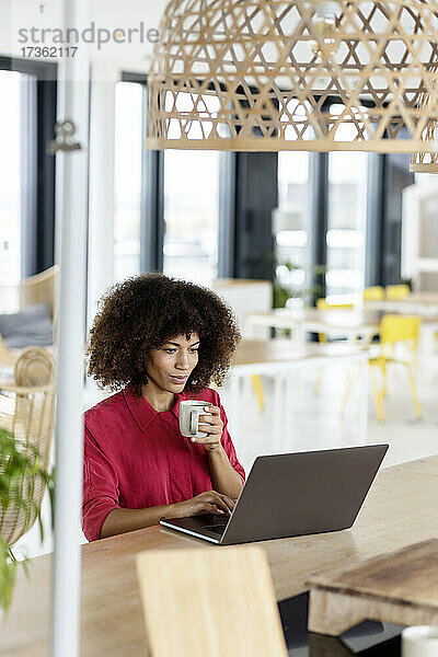 Berufstätige Frau trinkt Kaffee und benutzt einen Laptop im Büro