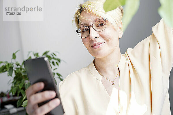 Blonde Frau hält Smartphone zu Hause