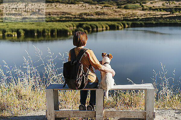 Frau mit Hund auf Bank in der Nähe des Sees sitzend