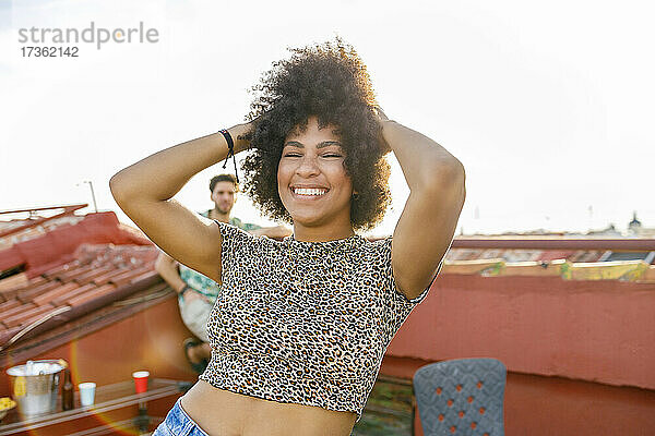 Fröhliche Afro-Frau tanzt mit den Händen im Haar auf dem Dach
