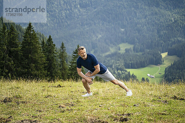 Mann streckt die Beine beim Sport auf einem Berg