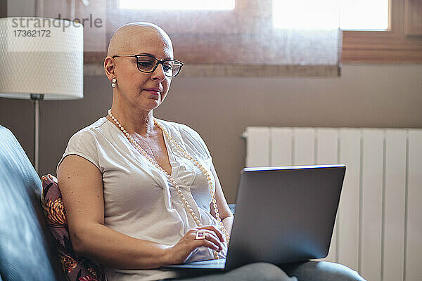 Glatzköpfige Frau benutzt Laptop im Wohnzimmer zu Hause