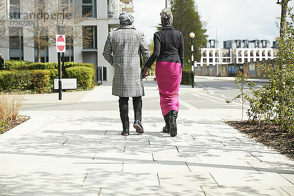 Paar hält sich an den Händen  während es an einem sonnigen Tag auf einem Fußweg spazieren geht