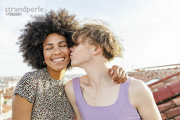 Junger Mann küsst Afro-Freundin auf die Wange auf dem Dach während einer Party