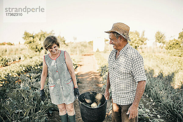 Lächelndes älteres Paar mit Gemüsekorb auf dem Bauernhof