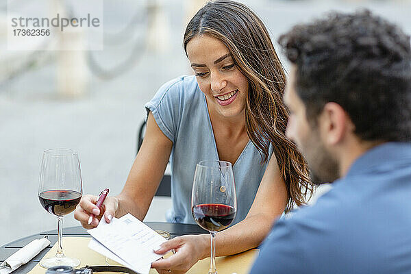 Lächelnde Frau zeigt ihrem Freund im Restaurant eine Postkarte