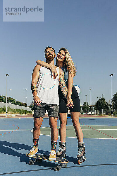 Lächelndes junges Paar hält sich am Basketballplatz an einem sonnigen Tag an den Händen