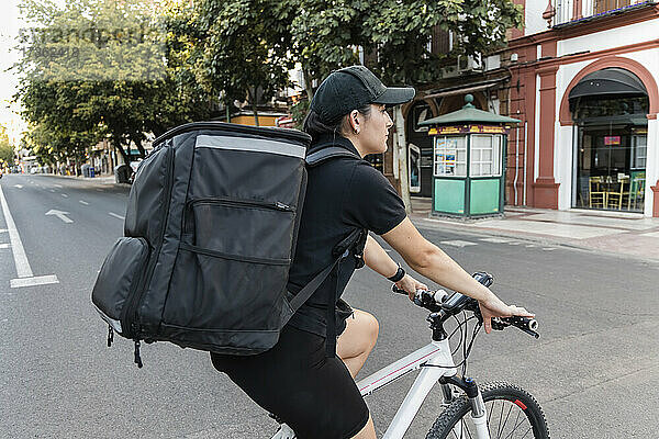 Weibliche Lieferperson mit Rucksack auf dem Fahrrad auf der Straße