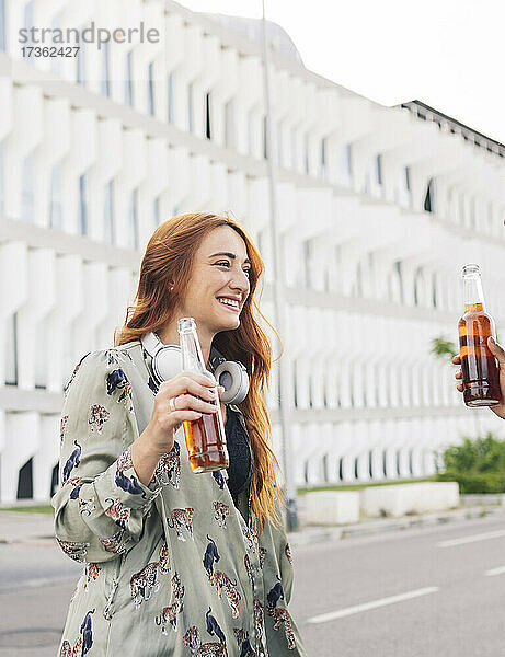 Lächelnde rothaarige Frau  die ihre Freundin anschaut  während sie ein Bier am Straßenrand genießt