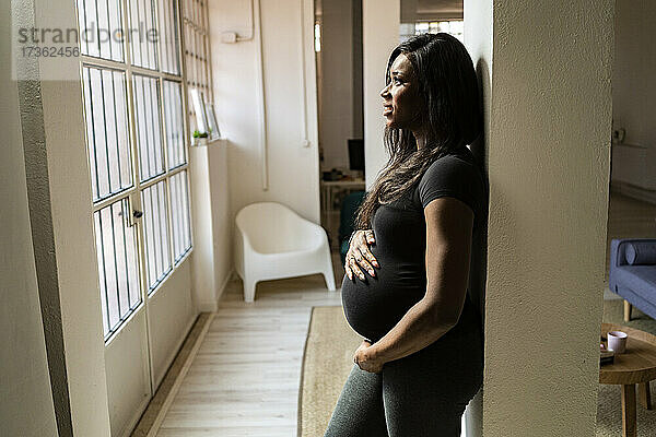 Nachdenkliche junge schwangere Frau  die sich zu Hause an eine Säule lehnt