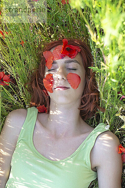 Mädchen mit Blütenblättern im Gesicht entspannt sich am Mohnfeld