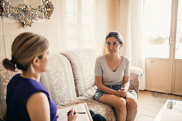 Junge Modedesignerin im Gespräch mit einem Kunden  während sie auf dem Sofa sitzt