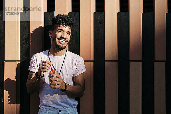 Lächelnder Mann mit Obstsalat  der wegschaut  während er vor einer Wand steht