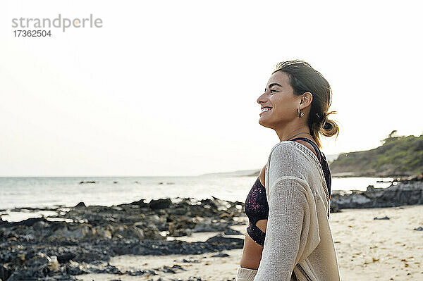 Lächelnde junge Frau mit Blick auf die Aussicht vom Strand