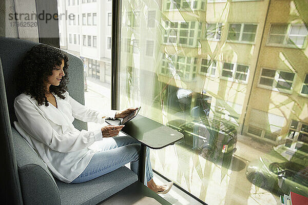 Weibliche Fachkraft  die ein digitales Tablet benutzt  während sie am Bürofenster sitzt