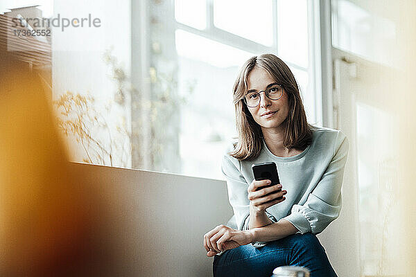 Junge Frau sitzt mit Mobiltelefon in einem Café