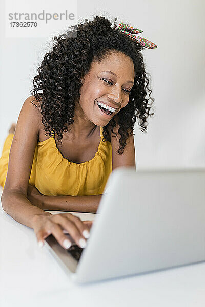Glückliche Afro-Frau  die einen Laptop benutzt  während sie auf weißem Hintergrund liegt