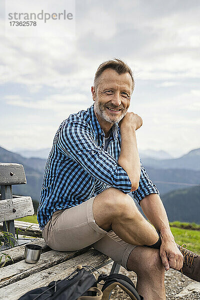 Lächelnder Mann sitzt mit übereinandergeschlagenen Beinen auf einer Bank