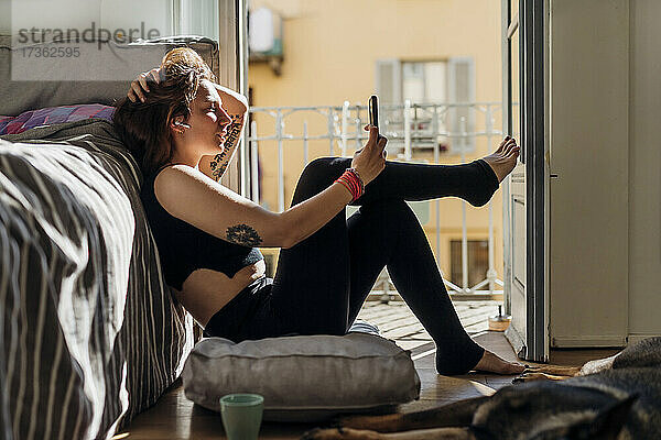 Frau mit Hand in den Haaren  die zu Hause ein Selfie mit ihrem Mobiltelefon macht