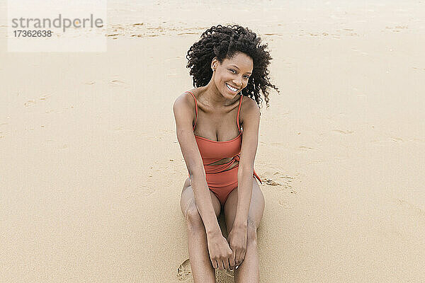 Glückliche schöne junge Frau sitzt auf Sand am Strand