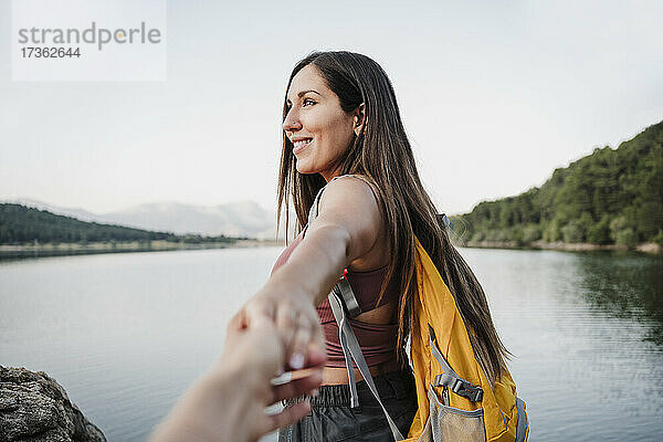Lächelnde Wanderin schaut weg  während sie die Hand eines Freundes am Seeufer hält