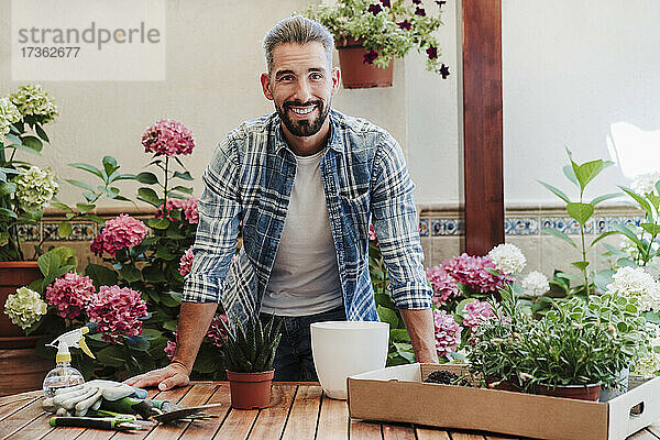 Lächelnder Mann mit Pflanzen auf einem Tisch im Hinterhof