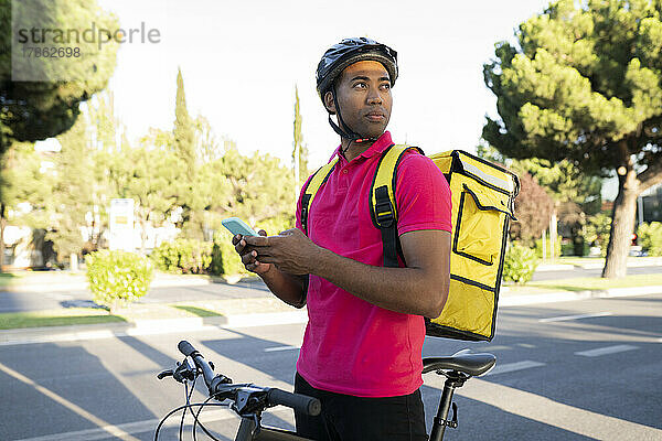 Zusteller  der sein Smartphone hält und wegschaut  während er mit dem Fahrrad steht