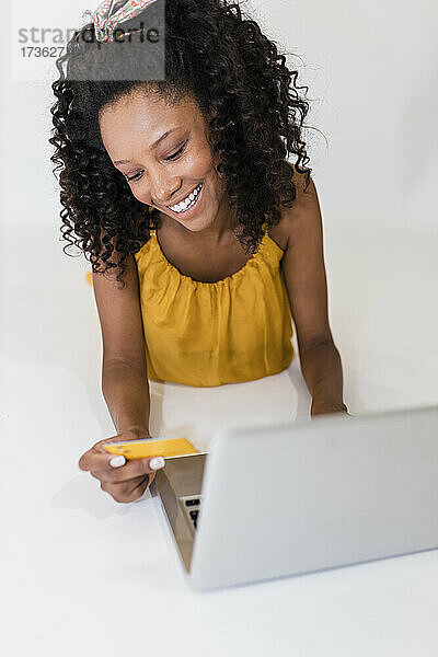 Frau hält Kreditkarte und benutzt Laptop auf weißem Hintergrund