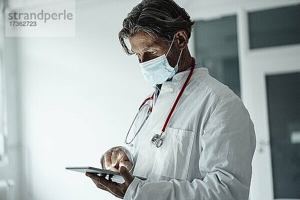 Älterer männlicher Mitarbeiter des Gesundheitswesens verwendet digitales Tablet im Krankenhaus während einer Pandemie