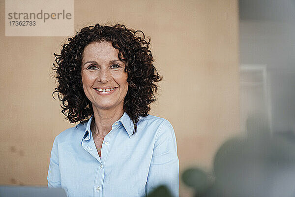 Lächelnde weibliche Fachkraft mit lockigem braunem Haar im Büro