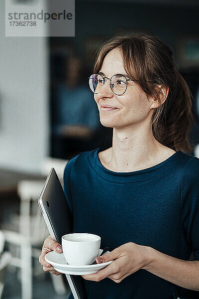 Lächelnde junge Geschäftsfrau mit Brille und Kaffeetasse in einem Café