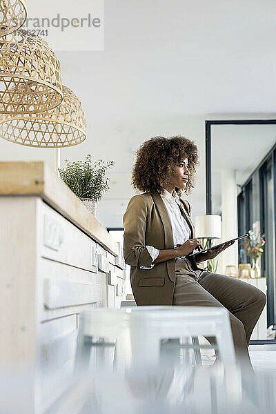 Junge Geschäftsfrau schaut weg  während sie mit einem digitalen Tablet im Büro sitzt