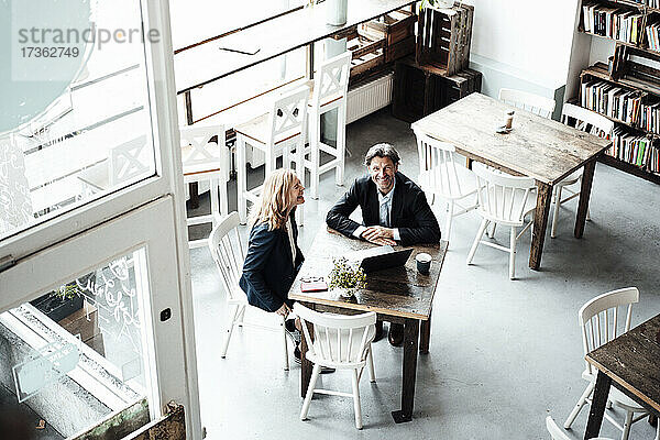 Glückliche männliche und weibliche Fachkräfte sitzen zusammen am Tisch in einem Café